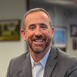 Smiling man in a gray suit indoors.